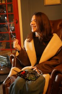 A beautiful woman sits in a comfortable armchair in Seknd Nature cannabis lounge while smoking a moonstick and smiling